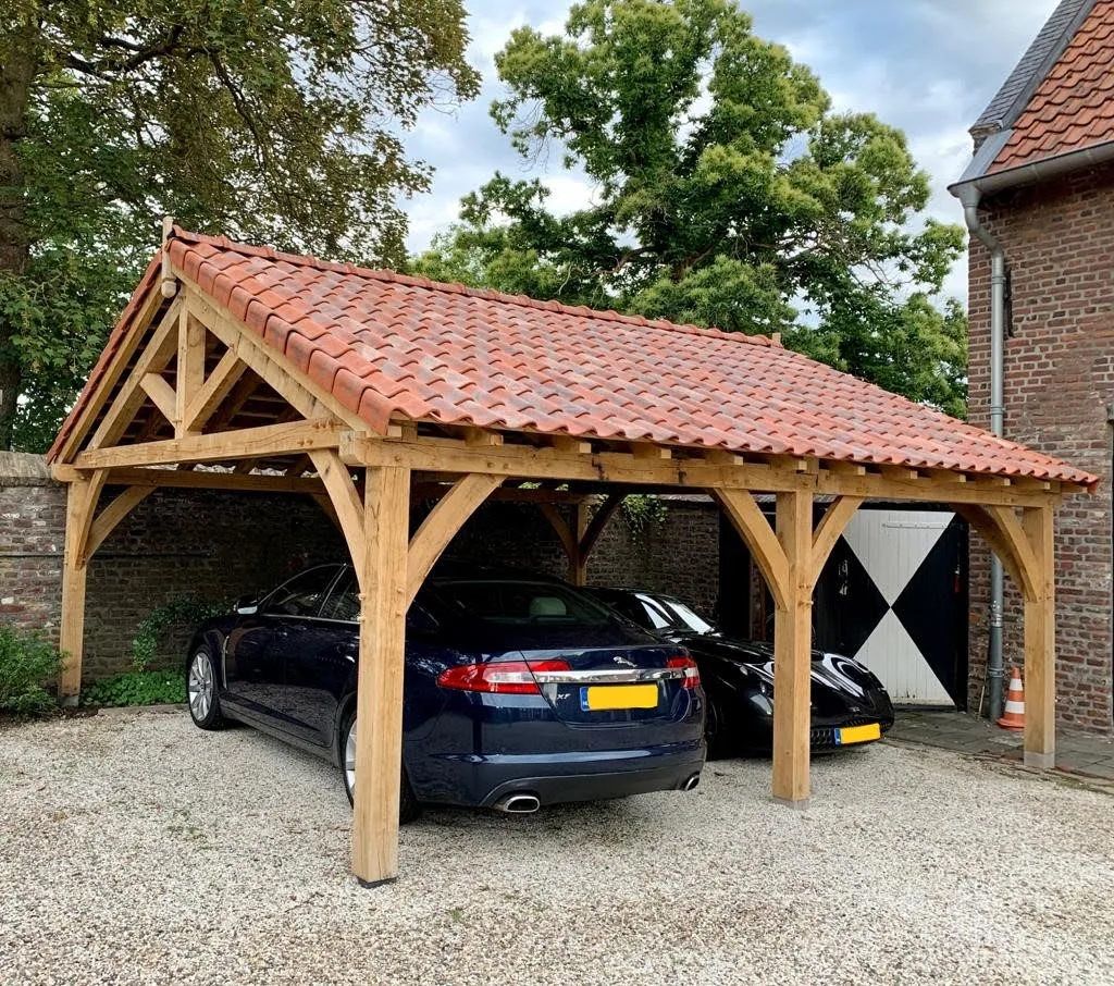 Zijaanzicht van de eiken carport met zichtbare gebintconstructie, naast de historische bijgebouwen van het landgoed