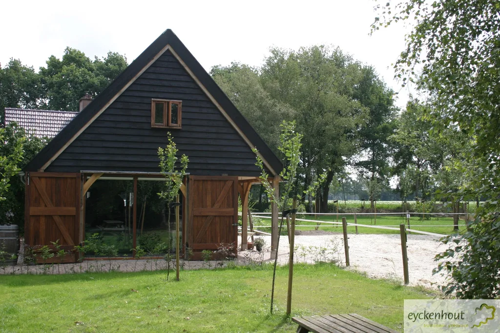 Gastenverblijf met zwarte gevel bij een paardenbak