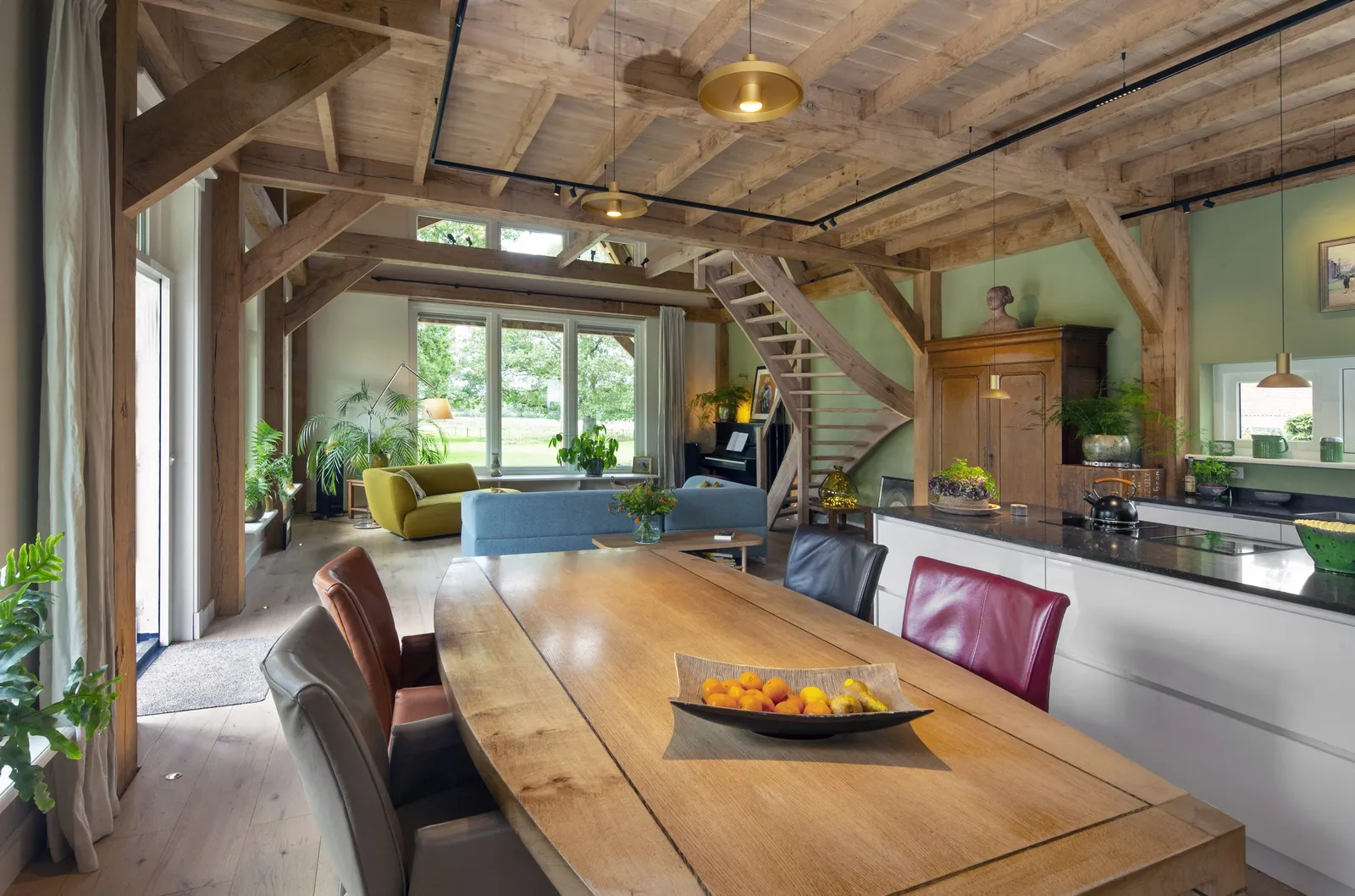 Eettafel onder het eiken balkenplafond, met de keuken en de trap erachter