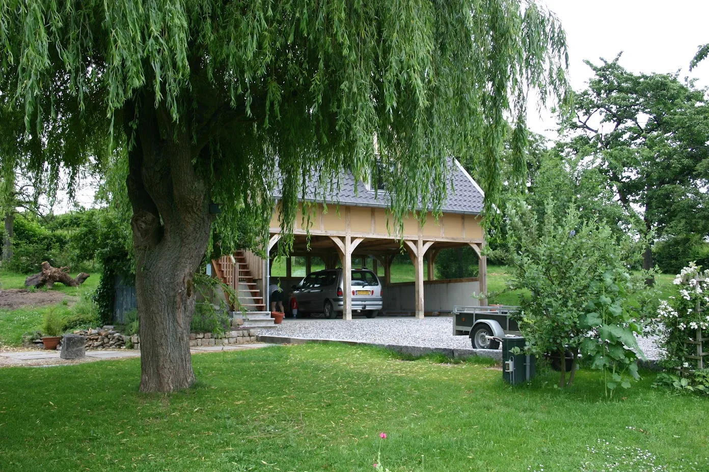 Eiken carport met gastenverblijf op de verdieping, onder een treurwilg